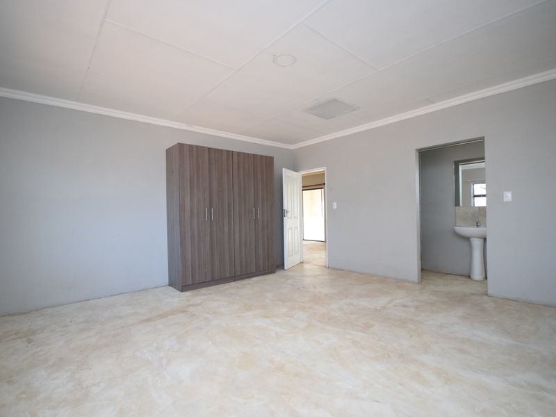 A spacious bedroom featuring a built-in wardrobe, an en-suite pedestal basin, and neutral grey walls, awaiting final flooring finishes.