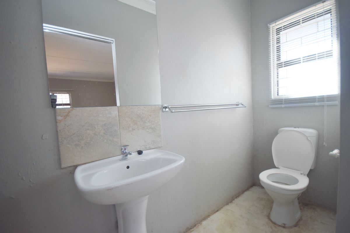 A functional bathroom featuring a pedestal basin, toilet, and wall-mounted mirror, requiring cosmetic updates to the flooring and wall finishes.