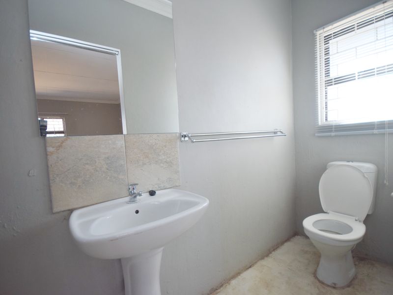A functional bathroom featuring a pedestal basin, toilet, and wall-mounted mirror, requiring cosmetic updates to the flooring and wall finishes.