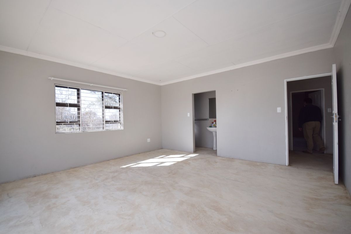 An empty bedroom featuring neutral walls, a coved ceiling, security bars on the window, and an adjoining en-suite area with a pedestal basin.