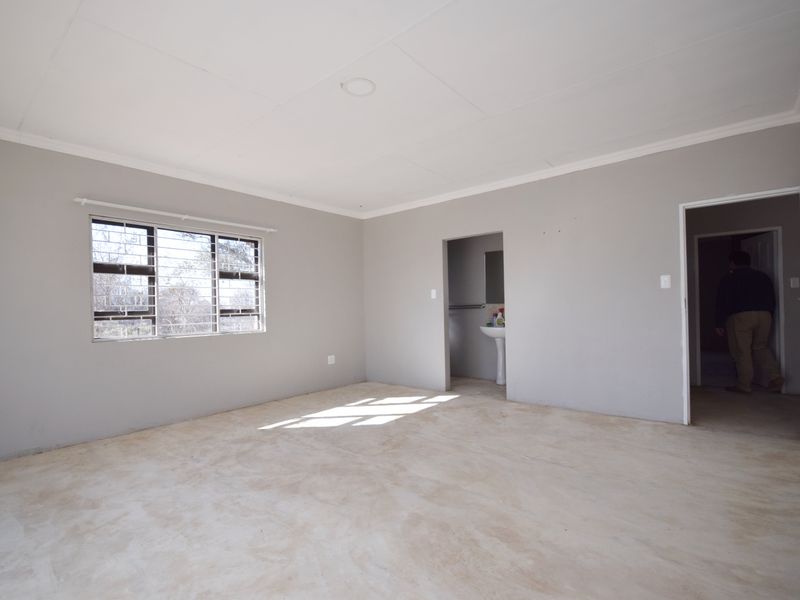 An empty bedroom featuring neutral walls, a coved ceiling, security bars on the window, and an adjoining en-suite area with a pedestal basin.