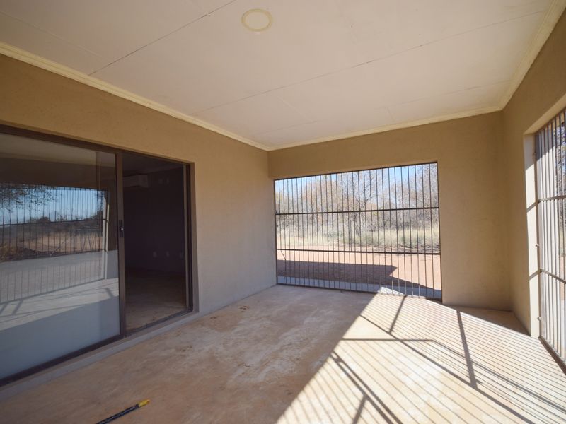 A covered patio area featuring concrete flooring, security bars, and a sliding glass door leading into the interior living space.
