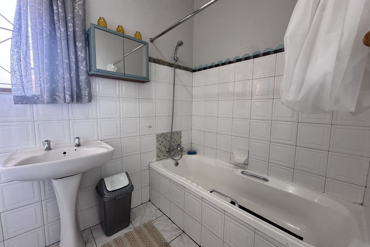A functional bathroom featuring a pedestal basin, a built-in bathtub with shower mixer, and classic white wall tiling.