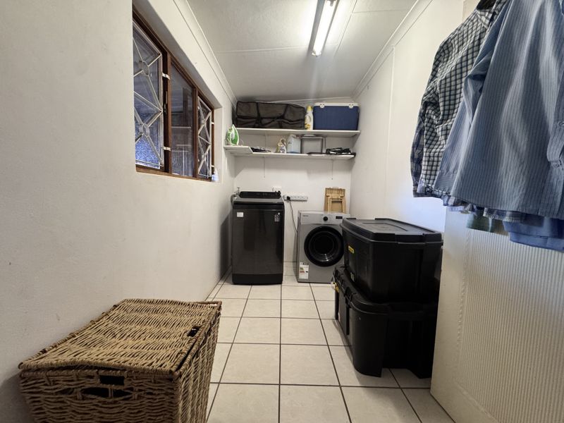 A functional laundry room featuring tiled flooring, built-in storage shelving, and security window bars, providing a practical space for household utility tasks.