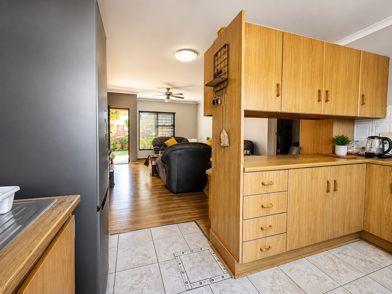 Open plan kitchen and living area featuring wood-look cabinetry, tiled kitchen flooring, and laminate wood flooring in the lounge with access to the garden.