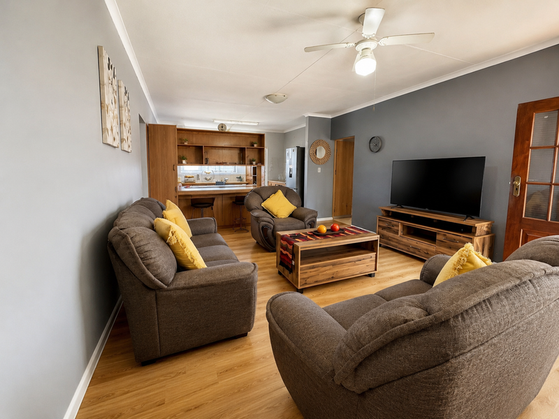 An open-plan living area featuring laminate flooring, a ceiling fan, and a functional kitchen with a breakfast bar and built-in cabinetry.