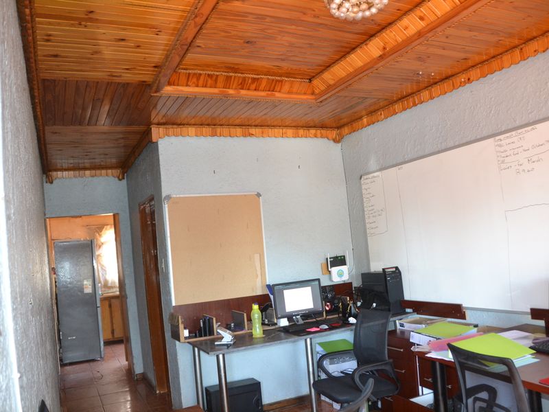 A functional home office space featuring a distinctive timber tongue and groove ceiling, textured walls, and tiled flooring, providing a practical workspace.