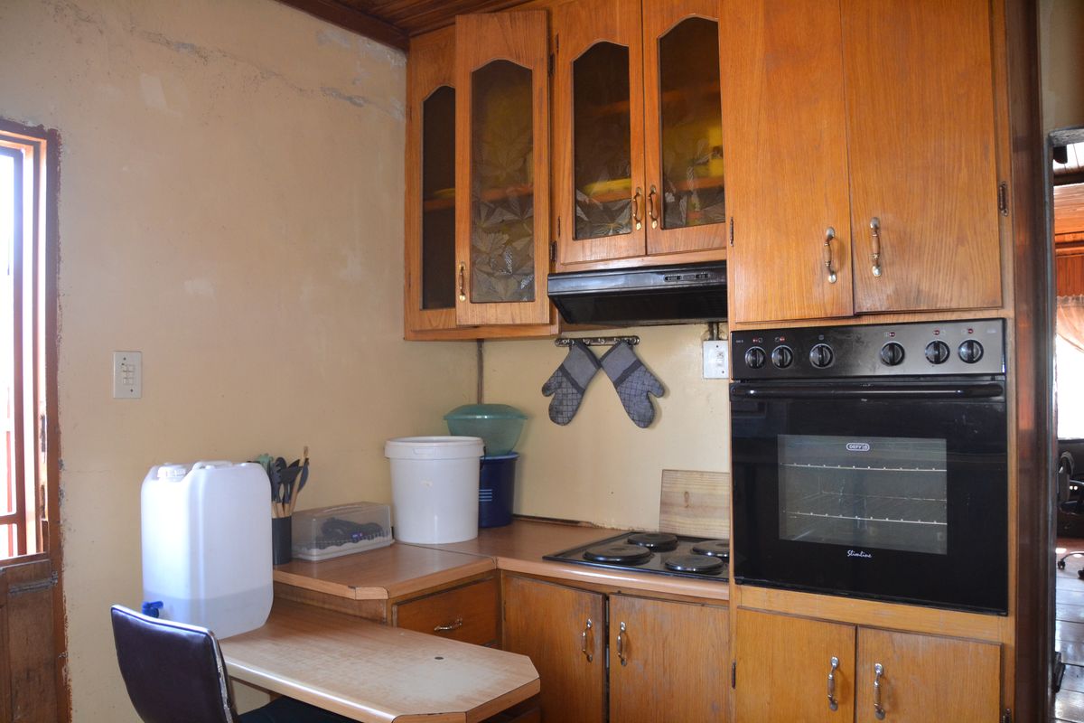 A dated kitchen featuring wooden cabinetry, built-in oven, electric hob, and extractor fan, requiring cosmetic updates to the walls and finishes.
