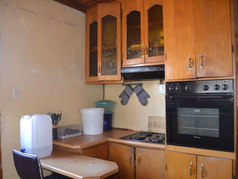 A dated kitchen featuring wooden cabinetry, built-in oven, electric hob, and extractor fan, requiring cosmetic updates to the walls and finishes.