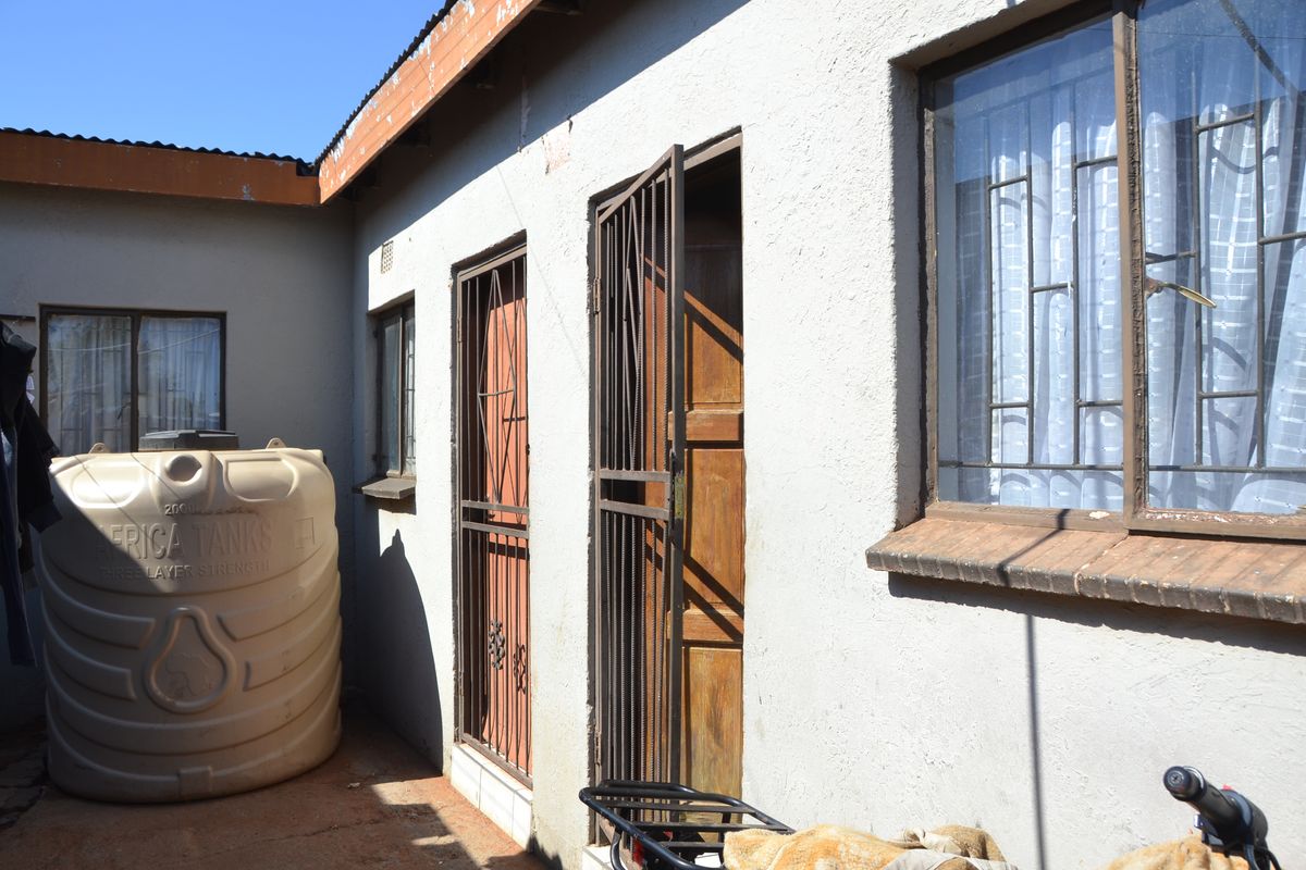 Rear exterior view of the property featuring a water storage tank, security gates on doors, and metal window frames.