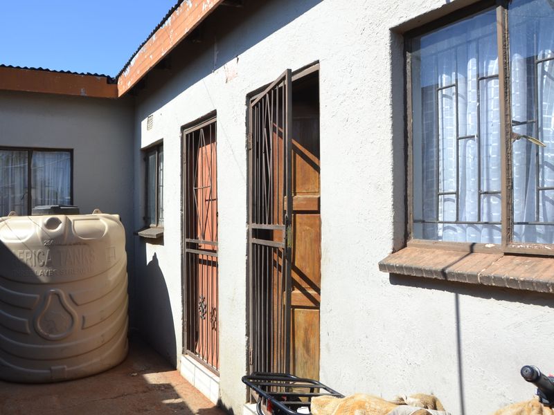 Rear exterior view of the property featuring a water storage tank, security gates on doors, and metal window frames.