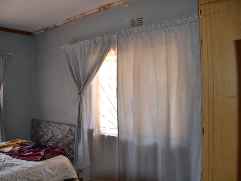 A bedroom featuring built-in wardrobes and security bars on the windows, currently requiring cosmetic updates to the walls and ceiling finishes.