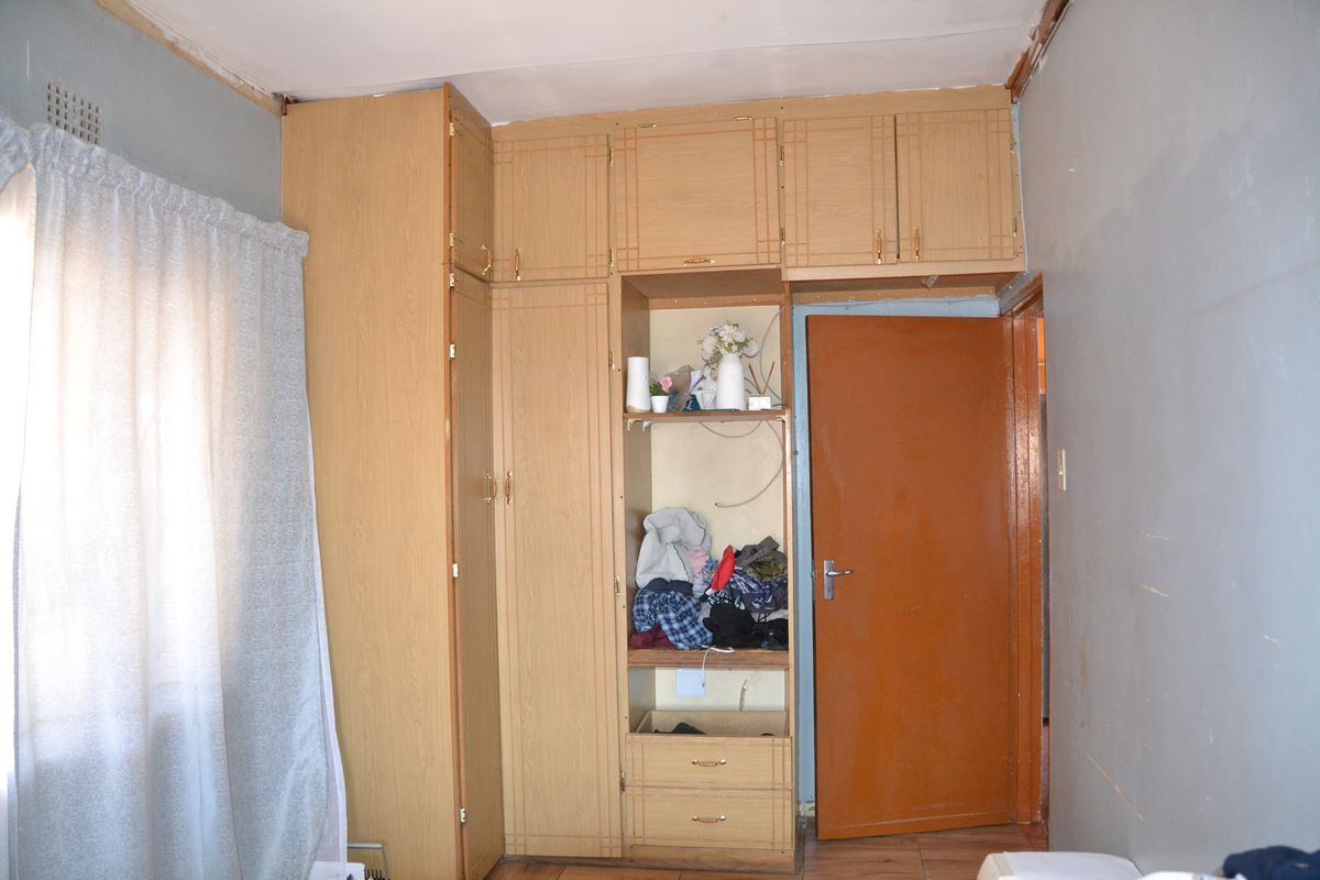 Bedroom featuring built-in wooden cupboards and laminate flooring, requiring cosmetic updates to the walls and ceiling finishes.