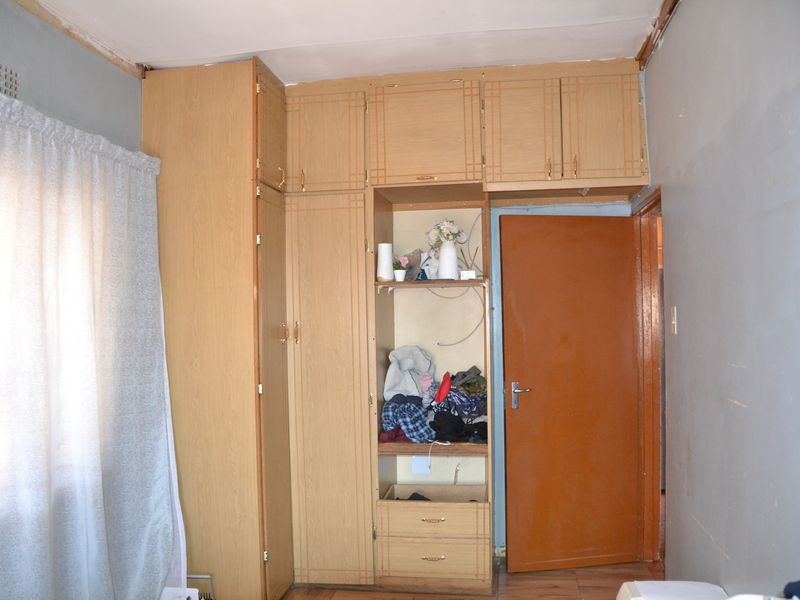 Bedroom featuring built-in wooden cupboards and laminate flooring, requiring cosmetic updates to the walls and ceiling finishes.