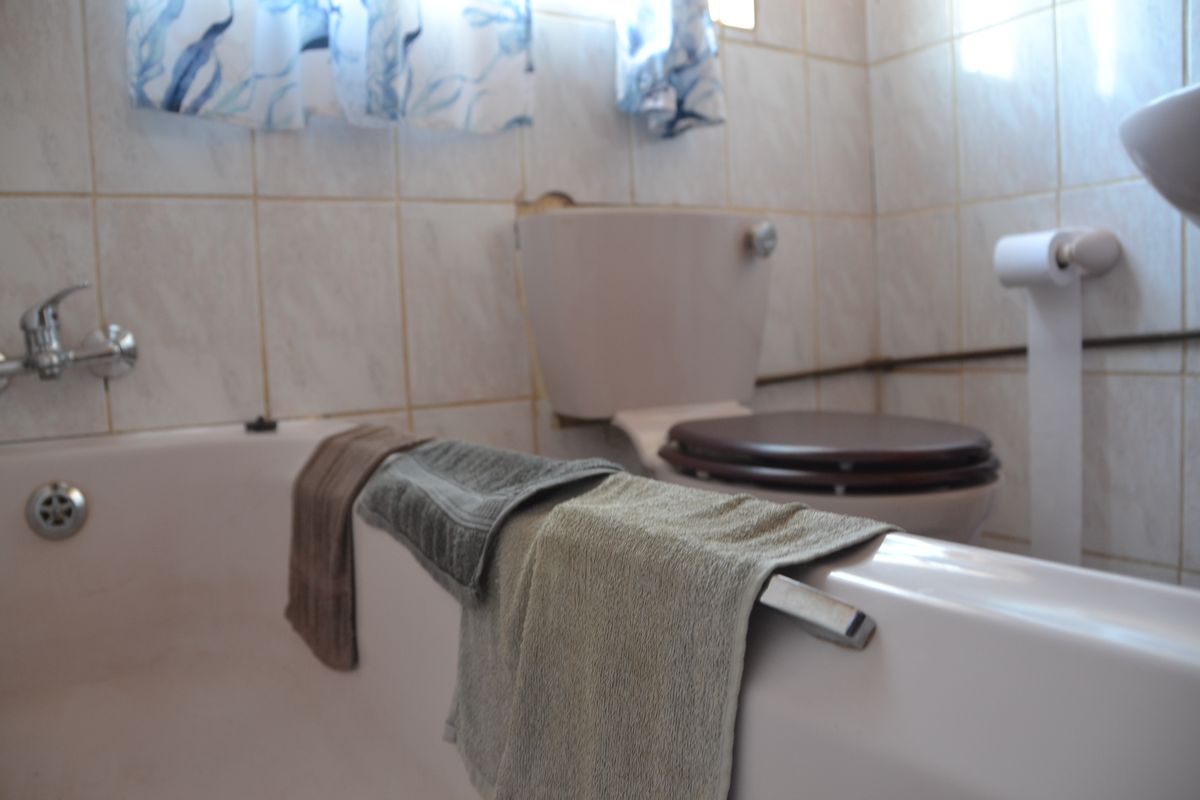A dated bathroom featuring a standard bathtub, toilet, and wall tiling, currently showing signs of wear and exposed plumbing.