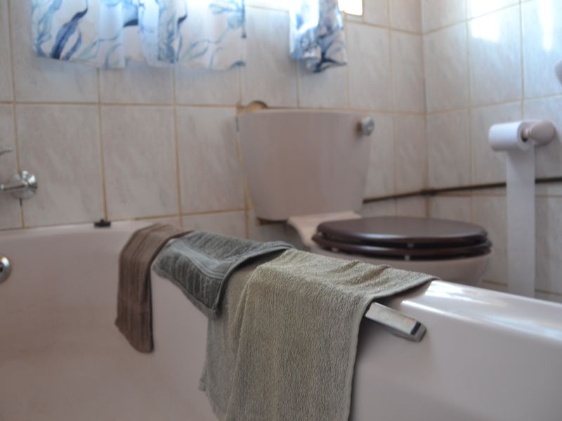 A dated bathroom featuring a standard bathtub, toilet, and wall tiling, currently showing signs of wear and exposed plumbing.