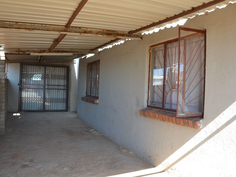 A covered outdoor patio area featuring a corrugated metal roof, security gates, and security bars on the windows.