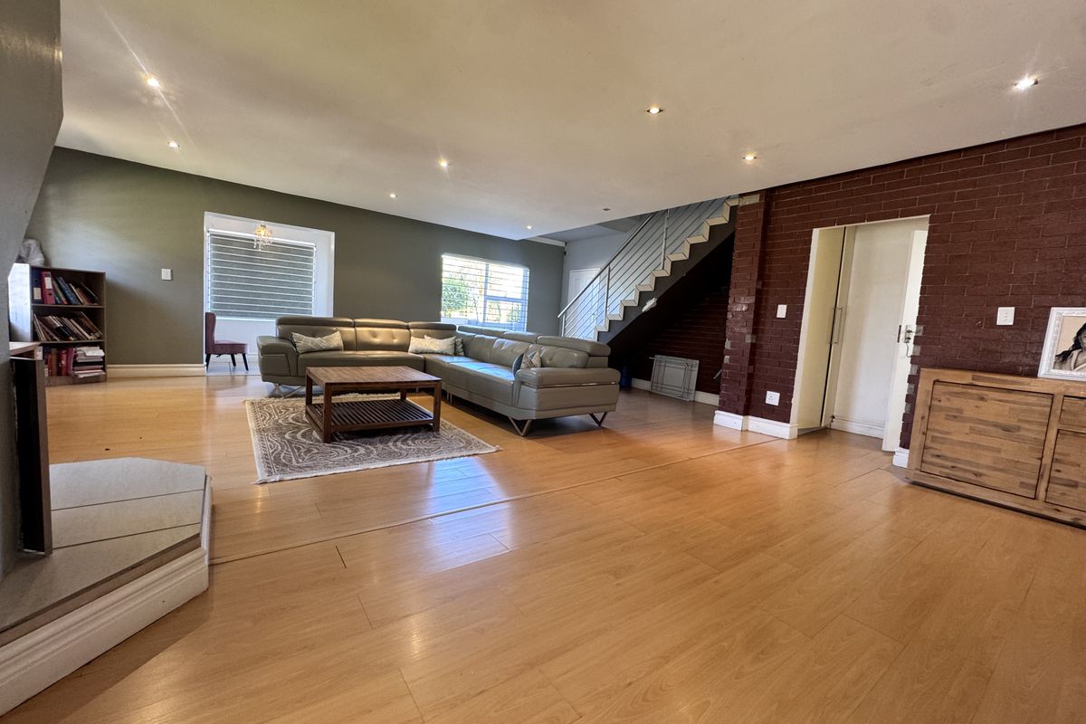 Spacious open-plan living area featuring laminate flooring, recessed lighting, a striking exposed brick wall, and a staircase with a modern metal railing.