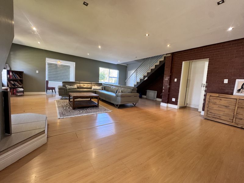 Spacious open-plan living area featuring laminate flooring, recessed lighting, a striking exposed brick wall, and a staircase with a modern metal railing.