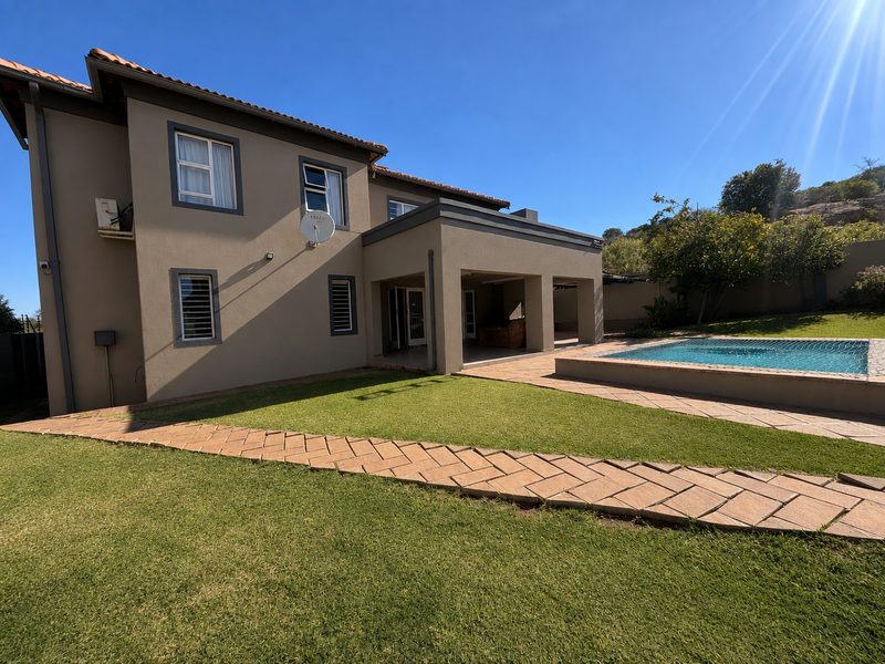 Rear view of the property featuring a well-maintained lawn, a paved walkway, a covered patio area, and a swimming pool.