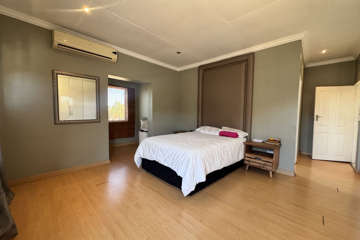 Spacious bedroom featuring laminate flooring, a built-in headboard, and a wall-mounted air conditioning unit.