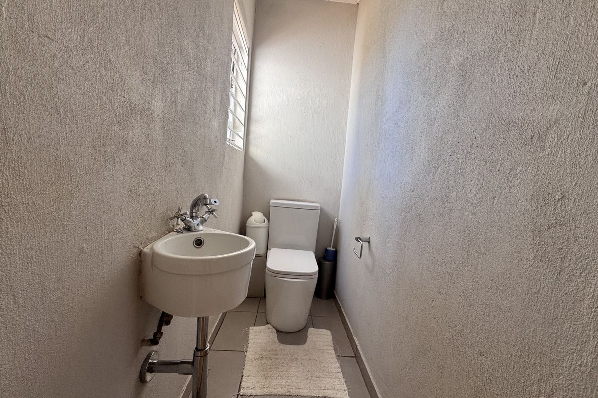 A compact guest bathroom featuring a wall-mounted basin, modern toilet, and tiled flooring with neutral wall finishes.