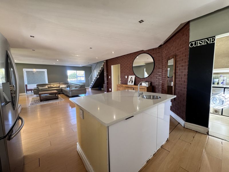 Open-plan living area featuring a kitchen island with sink, exposed brick wall, and staircase, flowing into a spacious lounge area with modern finishes.