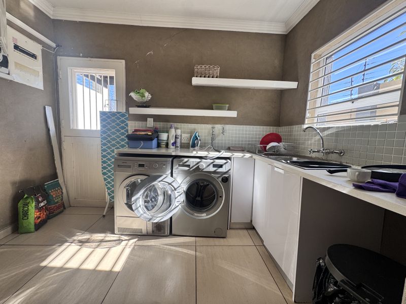 Functional laundry room featuring tiled floors, built-in cabinetry, a stainless steel sink, and floating shelving with direct access to the exterior.