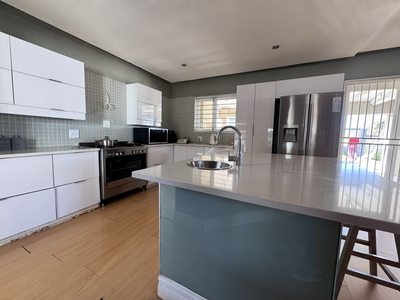 Modern kitchen featuring a central island with quartz countertops, stainless steel appliances, mosaic tile backsplash, and ample built-in cabinetry.