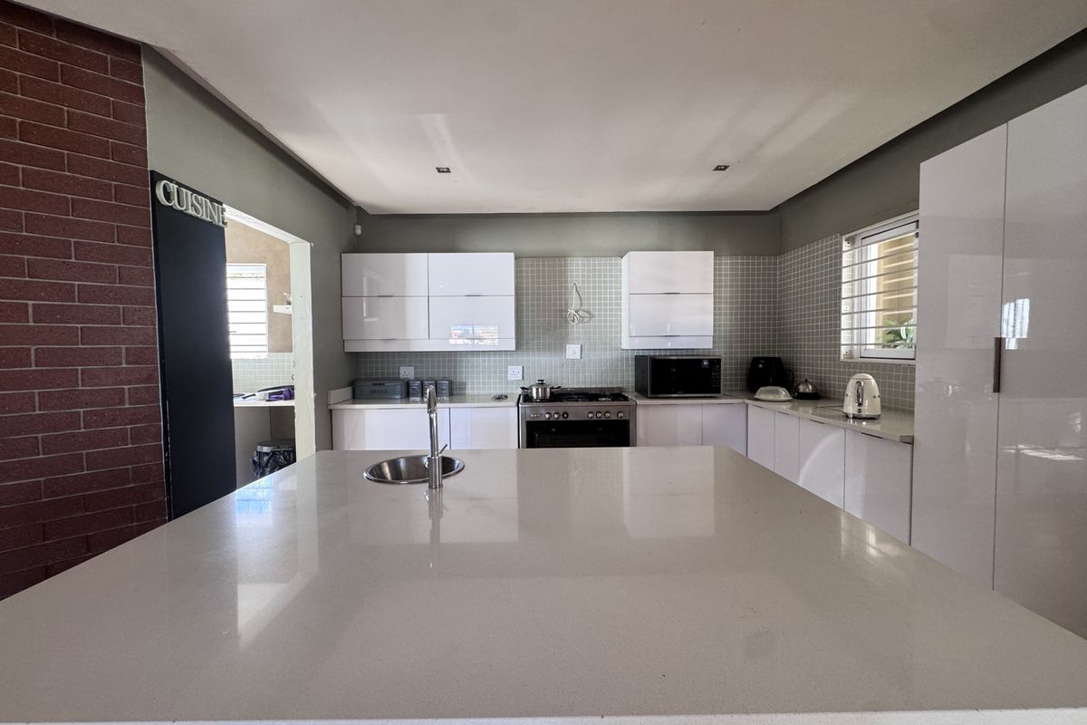 Modern kitchen featuring a large central island with stone countertops, glossy white cabinetry, tiled backsplash, and a striking exposed brick feature wall.