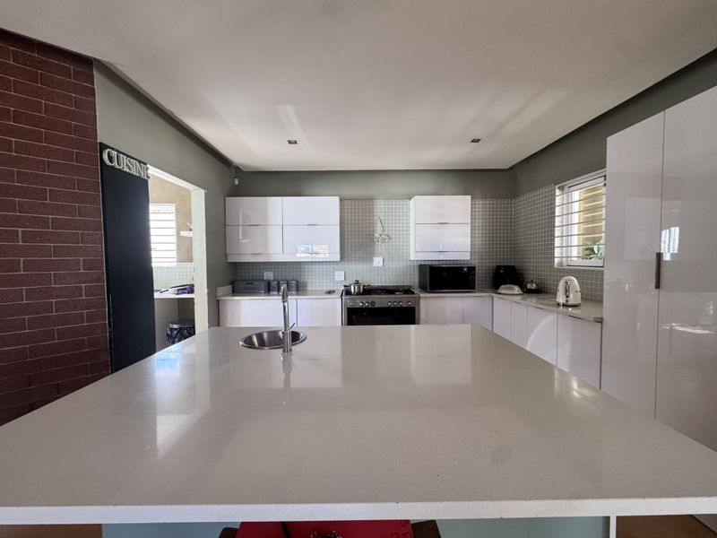 Modern kitchen featuring a large central island with stone countertops, glossy white cabinetry, tiled backsplash, and a striking exposed brick feature wall.