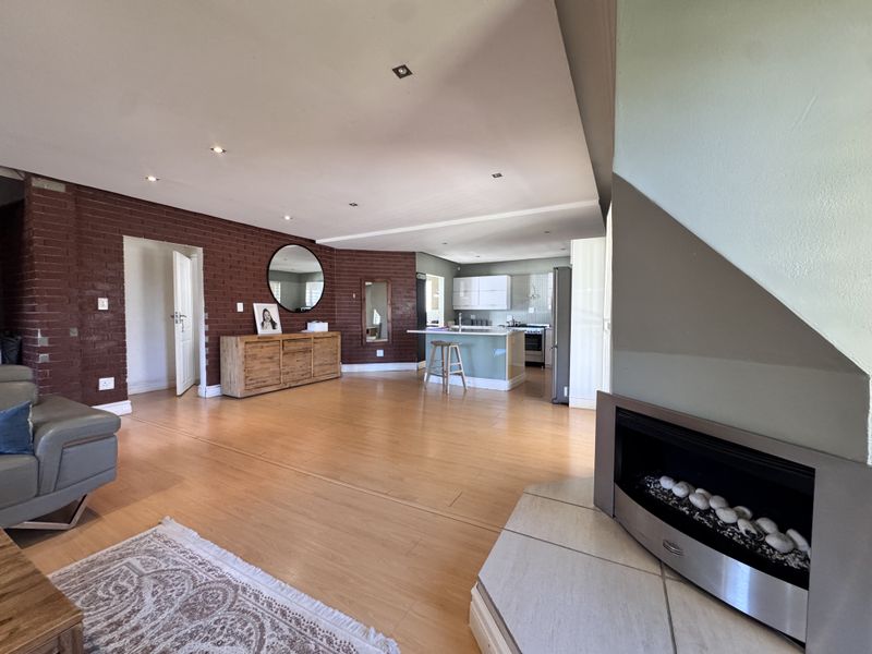 Spacious open-plan living area featuring a modern kitchen island, exposed brick feature wall, and a built-in fireplace with a tiled hearth.