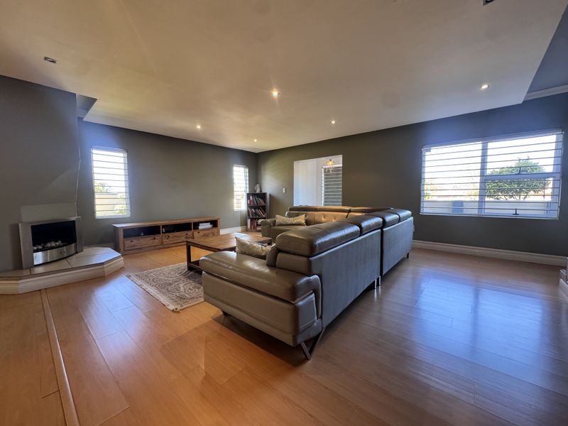 Spacious living room featuring laminate flooring, a built-in fireplace, and large windows with horizontal blinds, providing a comfortable and well-lit area.