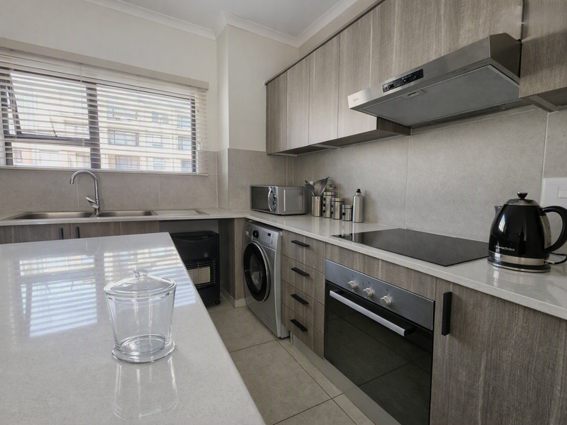 Modern kitchen featuring sleek wood-grain cabinetry, stone countertops, integrated appliances, and a functional layout with ample storage and a built-in oven and hob.
