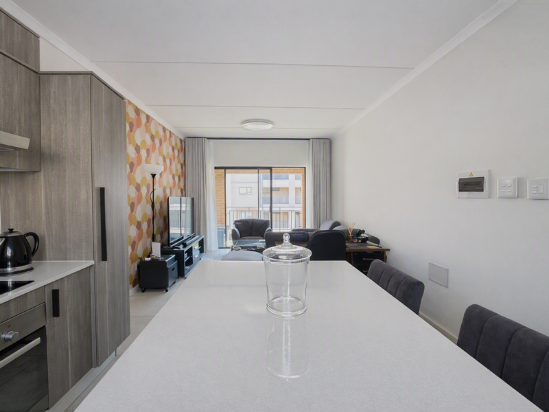 Modern open-plan kitchen and living area featuring sleek cabinetry, stone countertops, integrated appliances, and direct access to a private balcony.