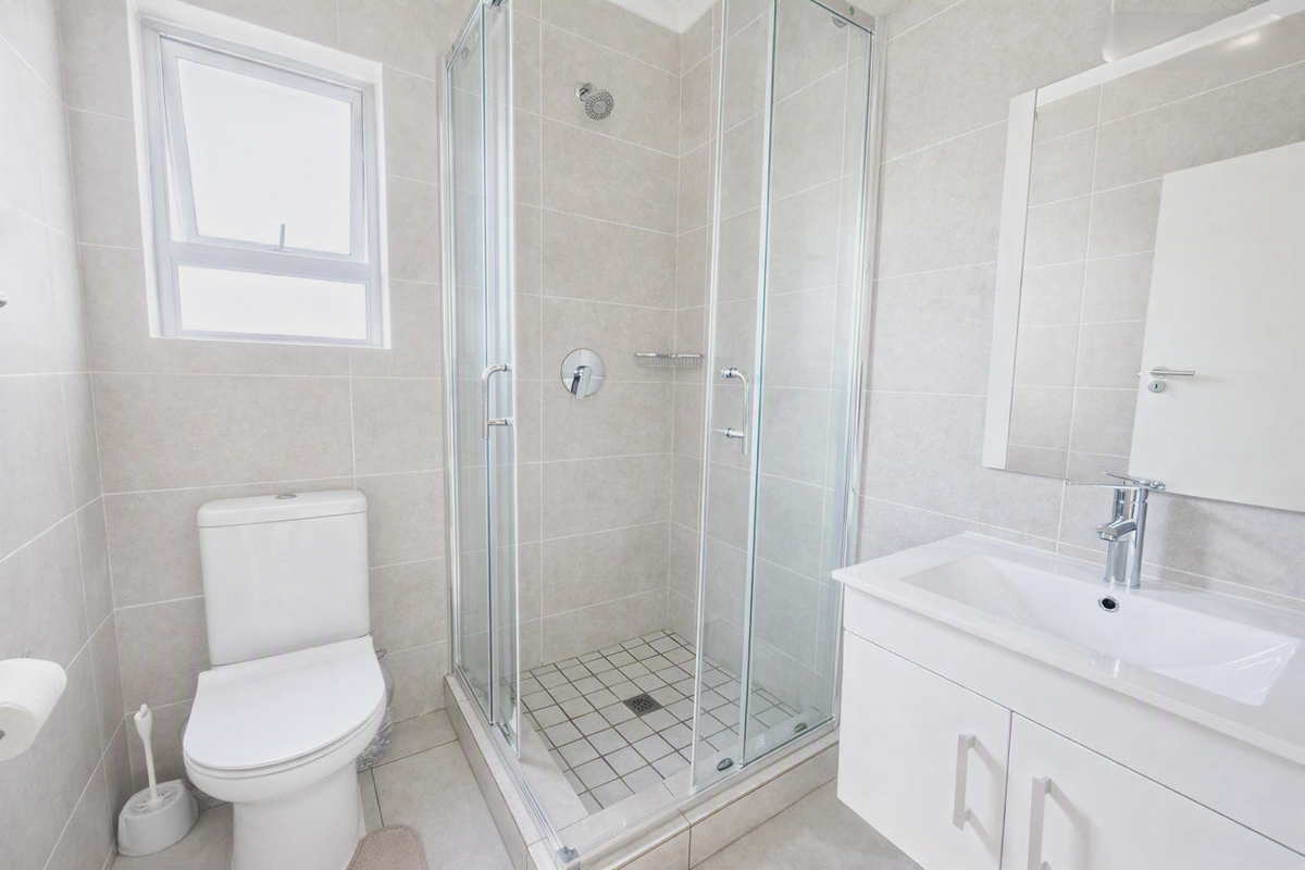 A clean, modern bathroom featuring a glass-enclosed shower, a white vanity with a basin, and neutral wall and floor tiling.