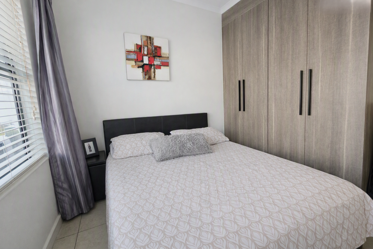 A well-maintained bedroom featuring neutral tiled flooring, modern wood-finish built-in cupboards, and venetian blinds for natural light control.
