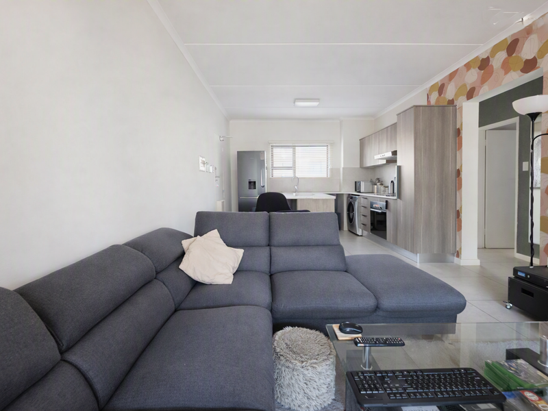 An open-plan living area featuring a modern kitchen with built-in cabinetry, integrated appliances, and neutral tiled flooring throughout the space.