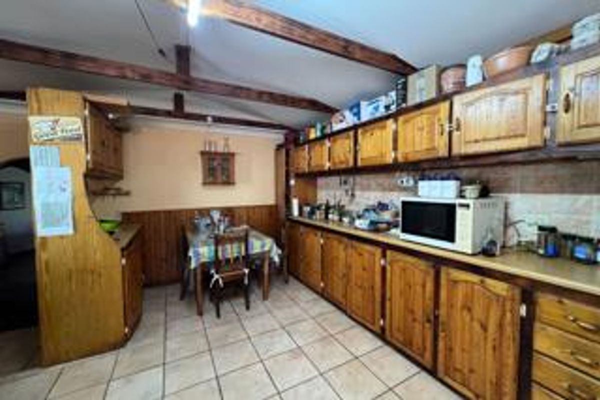 A dated kitchen featuring extensive wooden cabinetry, exposed ceiling beams, and tiled flooring, offering significant potential for a modern renovation.