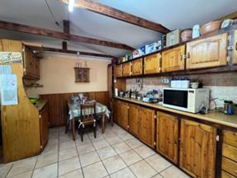 A dated kitchen featuring extensive wooden cabinetry, exposed ceiling beams, and tiled flooring, offering significant potential for a modern renovation.