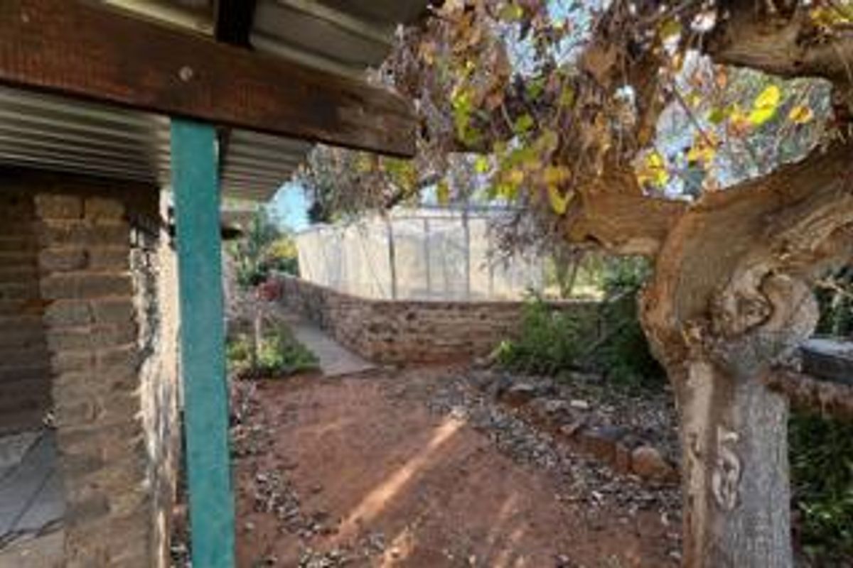 A view of the rear garden area featuring a brick structure, a covered patio section, and a greenhouse enclosure.