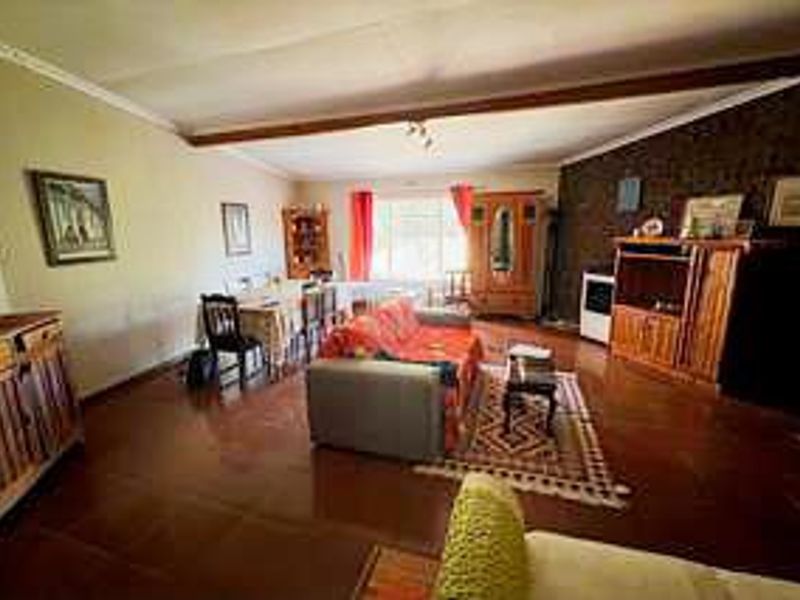 Spacious open-plan living and dining area featuring tiled flooring, an exposed ceiling beam, and a textured feature wall.