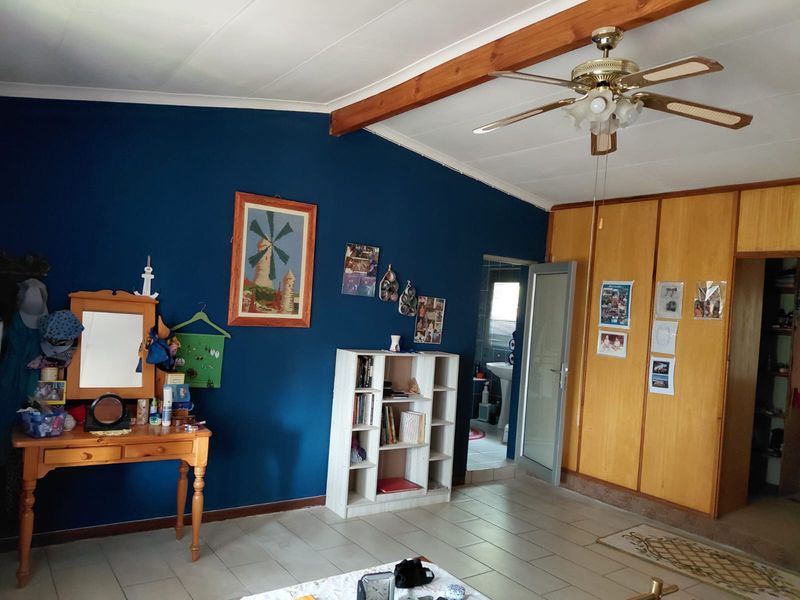 A bedroom featuring tiled flooring, built-in wooden cupboards, and an exposed timber ceiling beam with a central ceiling fan.