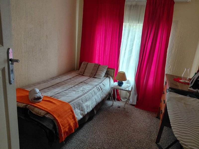 A compact bedroom featuring textured walls and carpeted flooring, providing a functional space with natural light.