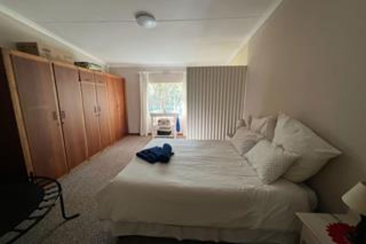 Spacious bedroom featuring extensive built-in wooden cupboards and neutral carpeting, offering a functional layout with ample storage space.