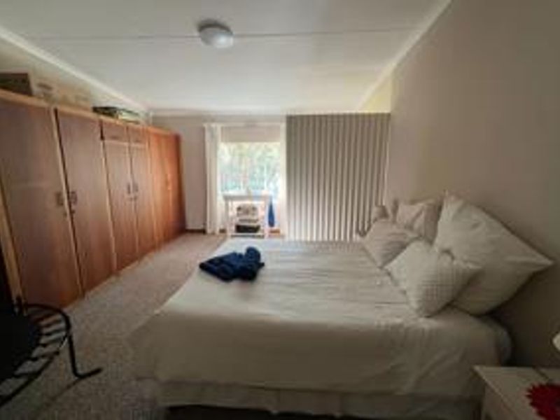 Spacious bedroom featuring extensive built-in wooden cupboards and neutral carpeting, offering a functional layout with ample storage space.