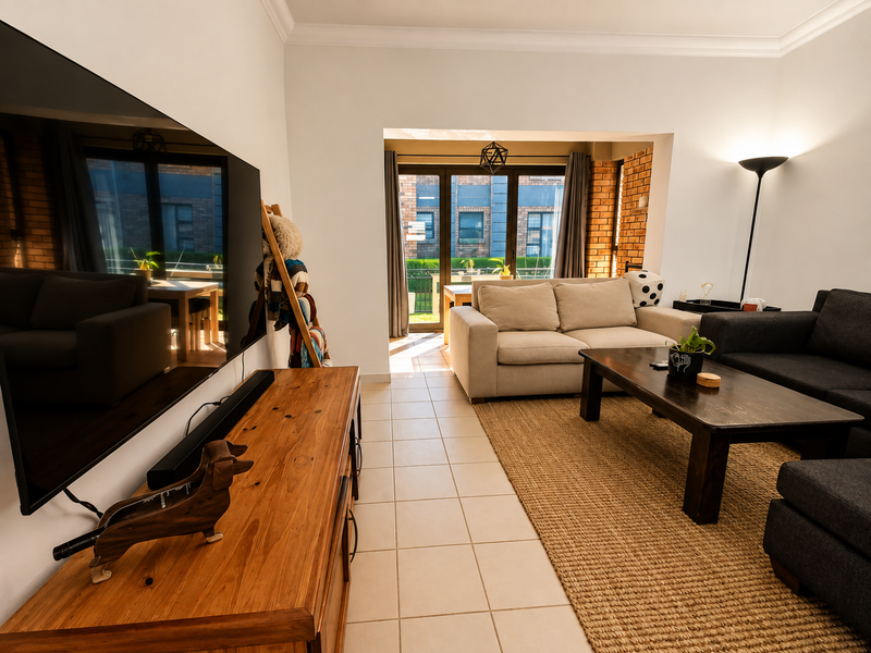 A bright living room featuring tiled flooring, exposed brick accents, and large sliding glass doors that provide natural light and access to the patio.