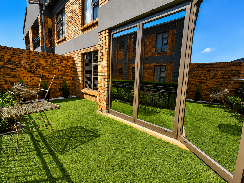 A private rear courtyard featuring low-maintenance artificial lawn, face brick boundary walls, and large aluminium sliding doors providing access to the townhouse interior.