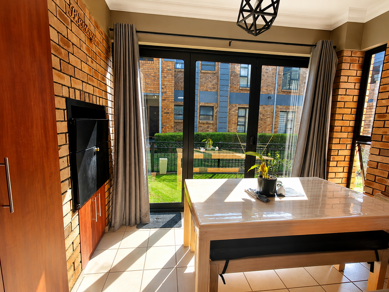 A bright living area featuring an exposed brick wall, built-in braai, and large sliding glass doors that open to a private garden view.