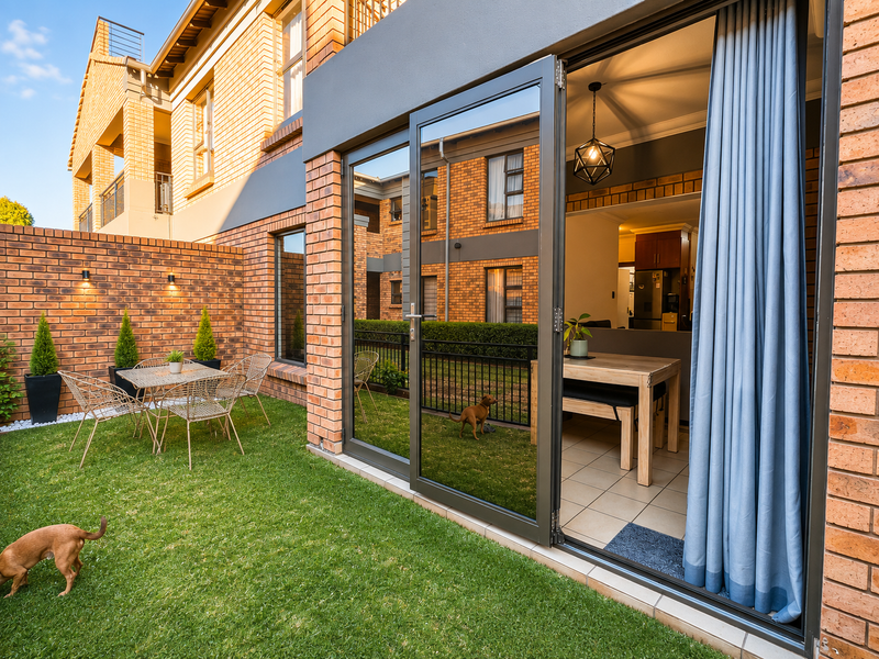 A well-maintained rear garden featuring a manicured lawn, face brick boundary wall, and large sliding glass doors leading into the interior living space.